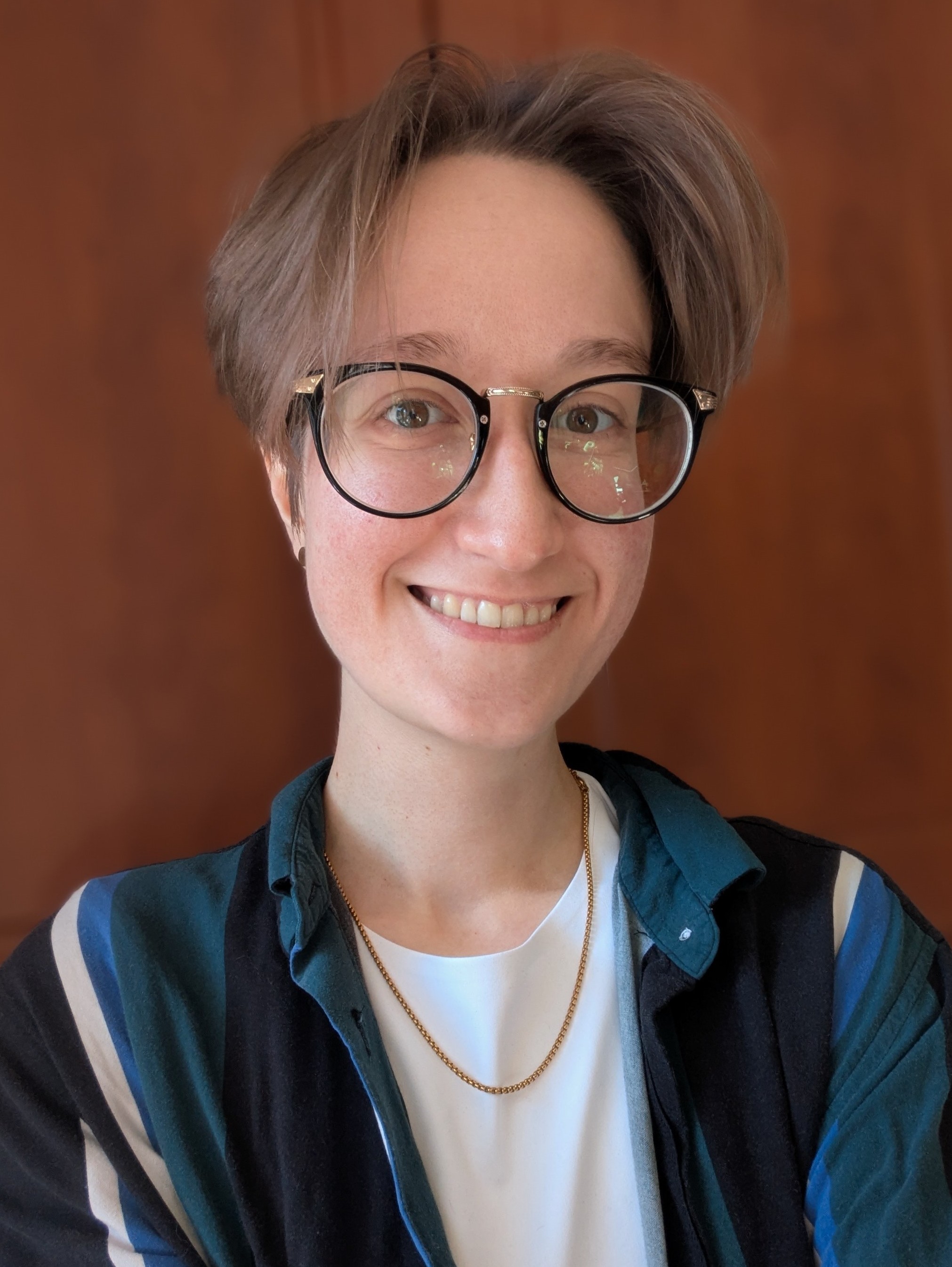 A person with short blonde hair and glasses smiling at the camera